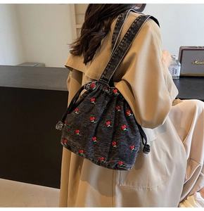 Detail of denim bucket bag featuring red cherry embroidery and a drawstring closure