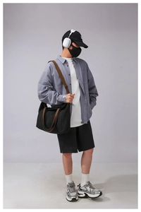 Model showing large black canvas tote bag with wide brown leather strap in studio