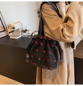 Close-up of black denim bucket bag with red cherry embroidery and drawstring detail