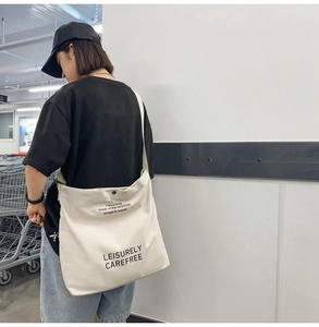 Detail of off-white canvas crossbody bag with black lettering and metal snap button closure