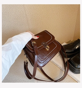 Gros plan sur le sac bandoulière en cuir marron avec surpiqûres et boucle dorée