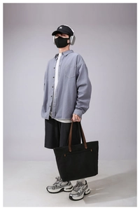 Detail of a large black canvas tote bag with brown leather handles on a lifestyle model