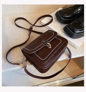Vue détaillée du sac bandoulière marron foncé avec surpiqûres blanches et fermoir doré
