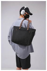 Detail of a large black canvas tote bag with brown leather handles worn over the shoulder