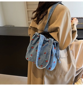 Detail of light blue washed denim bucket bag with embroidered cherry patterns on a model
