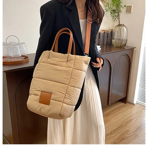 Detail of beige quilted puffer bucket bag with brown leather handle and wide strap