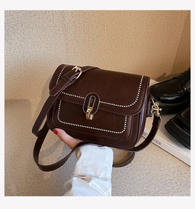 Détail du sac bandoulière en cuir marron foncé avec bordure perlée et fermoir doré rotatif