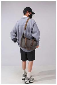 Detailed view of a large canvas tote bag with brown straps worn as a crossbody bag