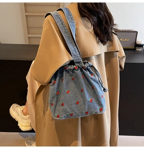 Detail of denim bucket bag featuring red cherry embroidery and drawstring closure