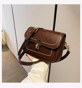 Détail du sac en cuir marron foncé avec bordures en perles blanches et fermoir doré