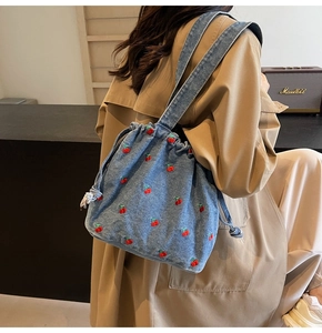 Detail view of denim bucket bag with red cherry embroidery and drawstring closure