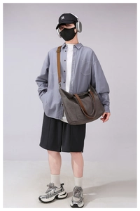 Model wearing a large dark grey canvas crossbody bag with contrast brown shoulder straps