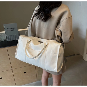 Detalle de bolsa de viaje blanca brillante con logo INOC y correa ajustable