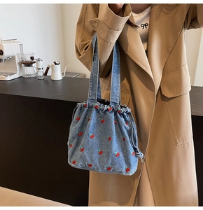 Detail view of denim bucket bag with cherry embroidery and drawstring closure