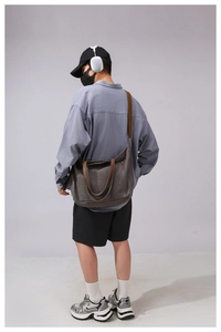 Rear view of a model wearing a large gray canvas tote bag with brown leather handles