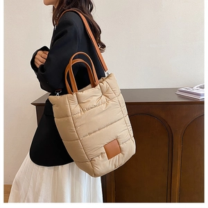 Quilted beige puffer bucket bag shown on shoulder with brown leather straps