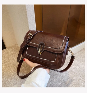 Détail du sac à bandoulière marron foncé avec coutures blanches et fermoir ovale doré