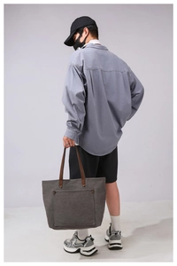 Large canvas tote bag with brown handles and front pocket shown on a model