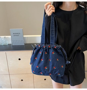 Detail of blue denim bucket bag with exquisite red cherry embroidery and drawstring