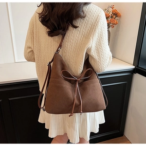 Detail of a dark brown suede bucket bag featuring a decorative leather bow and long strap