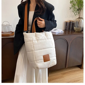 Detail view of cream quilted puffer tote bag with brown shoulder strap in a cozy interior