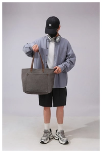 Detail of grey canvas tote bag with brown leather handles and front pocket with rivets