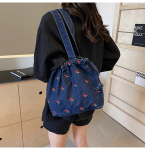 Detailed close-up of dark blue denim bucket bag featuring red cherry embroidery patterns