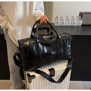 Detalle macro de la gran bolsa de viaje de cuero negro sobre una maleta blanca estriada
