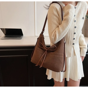 Close-up of brown suede tote bag featuring a decorative leather bow and side pocket detail