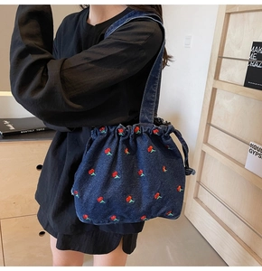 Detail of vintage denim bucket bag featuring cherry embroidery and drawstring closure
