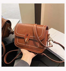 Gros plan d'un sac à bandoulière en cuir marron avec surpiqûres et fermoir doré ovale