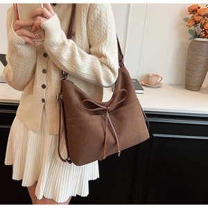 Detail of vintage brown suede hobo bag featuring decorative bow and adjustable strap