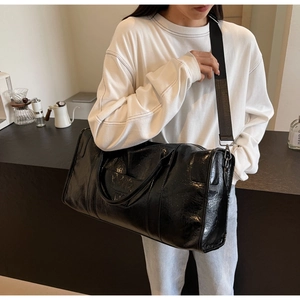 Detalle de bolsa de viaje en cuero negro brillante con bolsillo de cremallera y asa