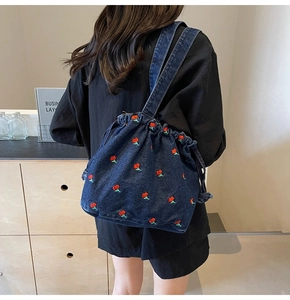 Detail of blue denim bucket bag with red cherry embroidery and drawstring closure