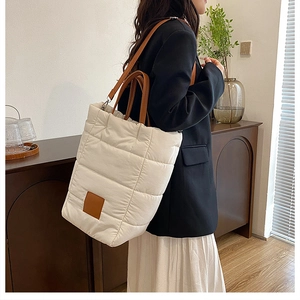 Detail of a creamy quilted bucket bag with brown handles on a model in a cozy setting