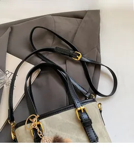 Detail of adjustable shoulder strap and buckle on a beige canvas and black leather bag