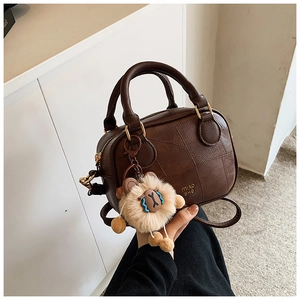 Detail of dark brown leather Boston bag with stitching details and lion plush charm