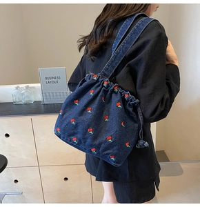 Detail of denim bucket bag with red cherry embroidery and drawstring closure