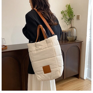 Detail showing white quilted fabric texture and brown leather strap on the bucket bag