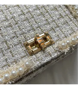 Detail of white tweed fabric with gold threads, pearl trim and golden metal lock buckle