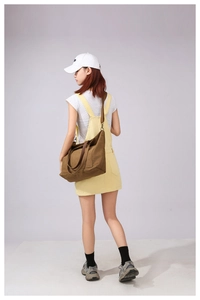 Large dark brown canvas tote bag shown on model with wide strap and spacious design