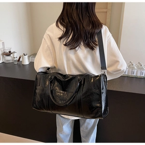 Detalle de bolsa de viaje grande en cuero negro con correa ancha y acabado texturizado