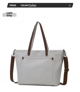 Detalle del bolso tote de lona gris claro con correas marrones y remaches metálicos