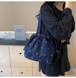 Close-up of dark denim bucket bag featuring detailed cherry embroidery and drawstring