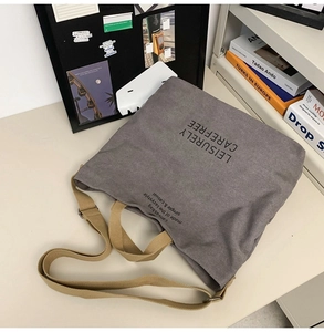 Detailed close-up of grey canvas tote bag with brown strap and artistic text print