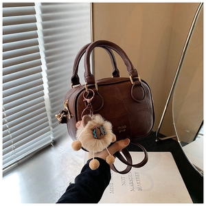 Detail of dark brown leather Boston bag with gold logo and plush lion charm accessory