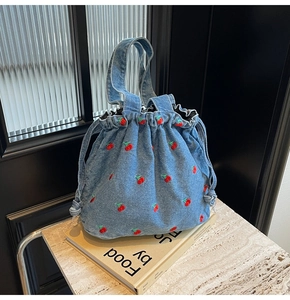 Macro view of light blue denim bucket bag featuring delicate red cherry embroidery