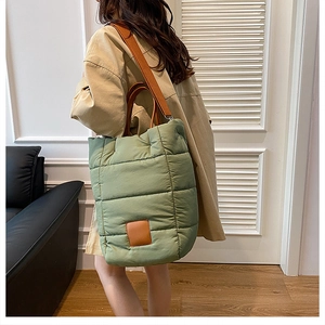 Model wearing a large green quilted nylon bucket bag with wide brown shoulder straps