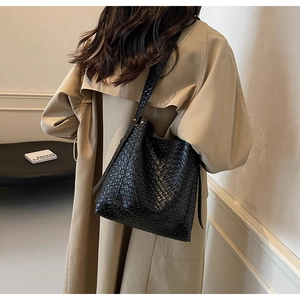 Vue détaillée d'un sac cabas noir tressé porté avec un trench-coat d'automne élégant