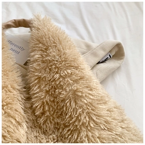 Detail shot of a plush beige tote bag featuring soft faux fur and brown leather handles